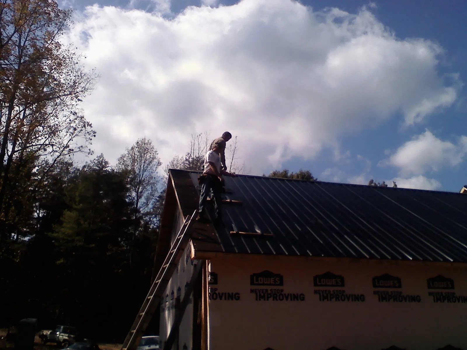 Roofer fastening dark metal panels high against a cloudy sky, from a Roof Inspection job in Butler